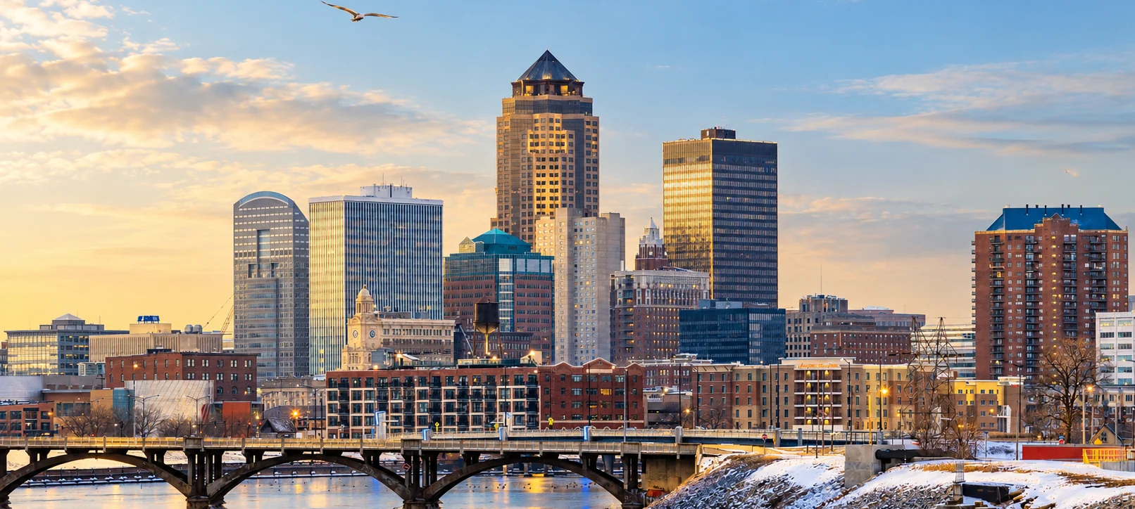 Des Moines skyline above the river and a snow-covered riverbank in warm morning light